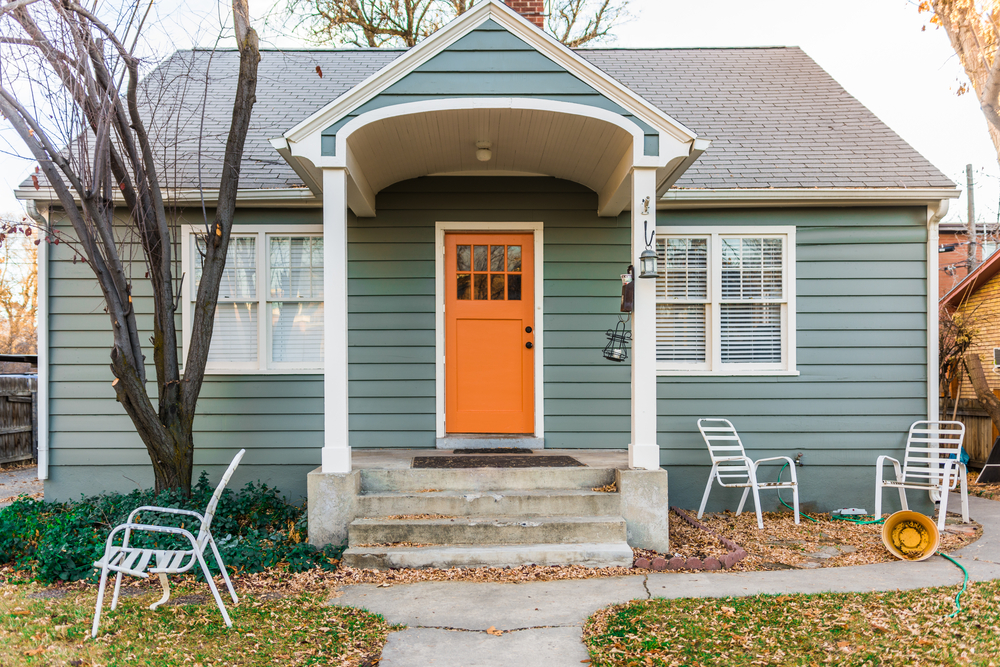 The front of a small house with a green exterior and a bright orange front door