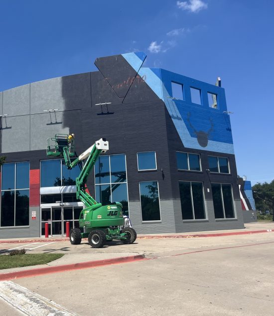 Bowlero to Lucky Strike Rebrand - painter in bucket truck repainting building side black.