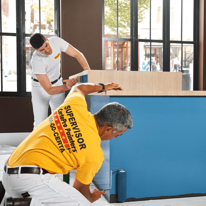 CertaPro Painters painter using a paint roller to paint a cabinet blue